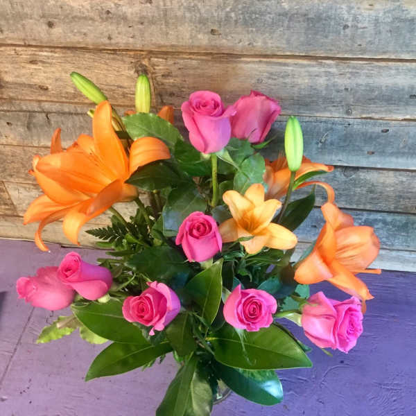 Arrangement of orange lilies and bright pink roses in a clear glass vase