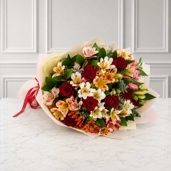Bouquet of red roses and pink alstroemeria wrapped in pale paper