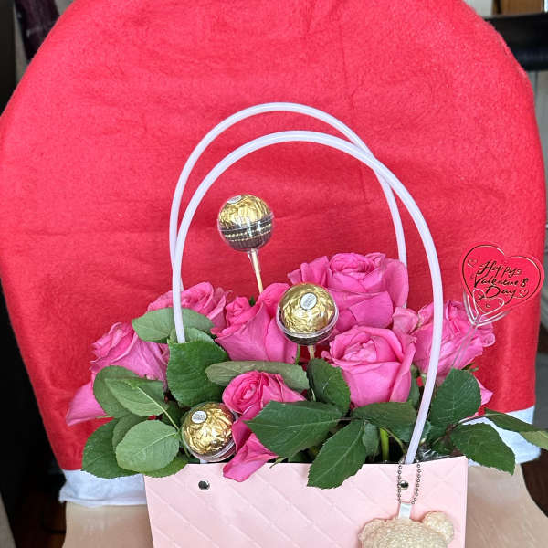 Pink roses in a gift bag with chocolates and a teddy bear charm
