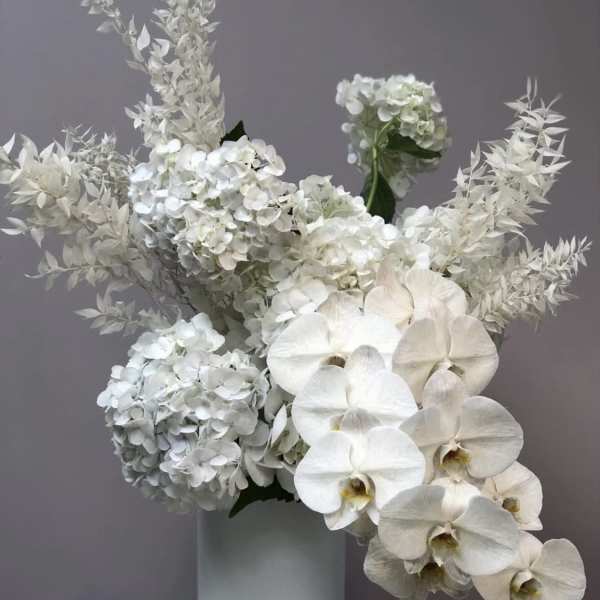White hydrangeas and orchids arranged in a tall vase