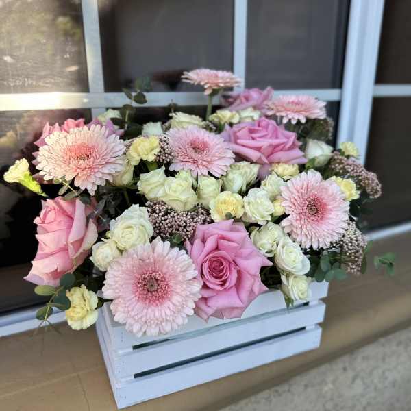 Pink roses and gerbera daisies arranged in a white wooden crate