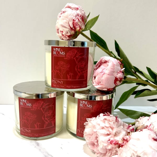 Three peony-scented candles with pink peony blooms arranged around them