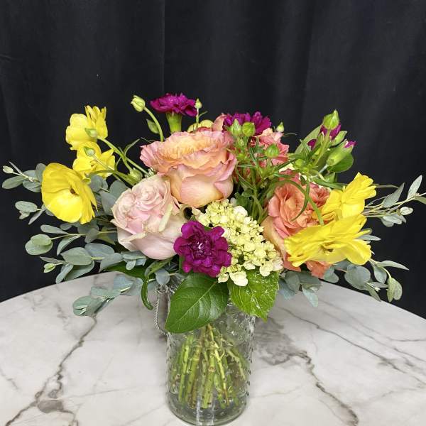 Mixed bouquet of pink, yellow, and peach flowers in a glass vase