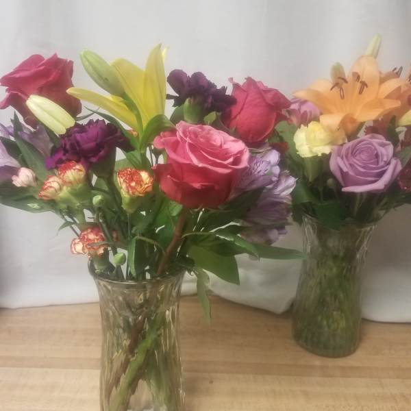 Two mixed flower bouquets in clear glass vases with roses and lilies