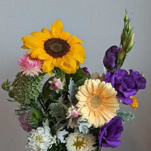 Mixed bouquet with sunflowers, purple blooms, and daisies in a glass vase