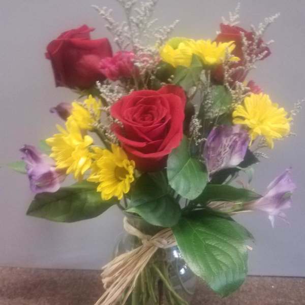 Bouquet of red roses, yellow daisies, and purple flowers in a glass vase
