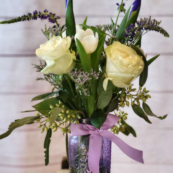 White roses and tulips in a purple glass vase with a lavender ribbon