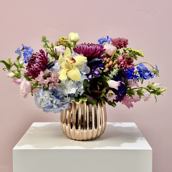 Mixed bouquet in a ribbed metallic vase with blue, pink, purple, and yellow flowers