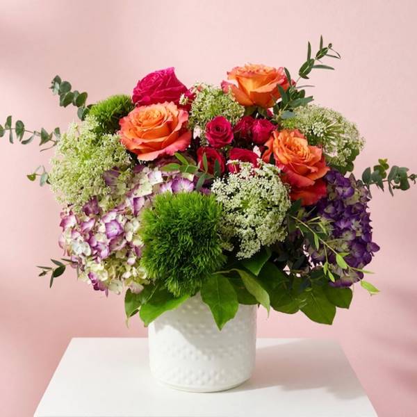 Mixed bouquet of orange and pink roses in a white vase