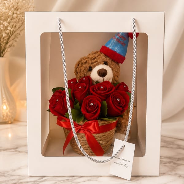 Teddy bear in a gift box with red roses and a birthday hat