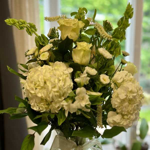 White floral arrangement in a clear glass vase with a ribbon bow