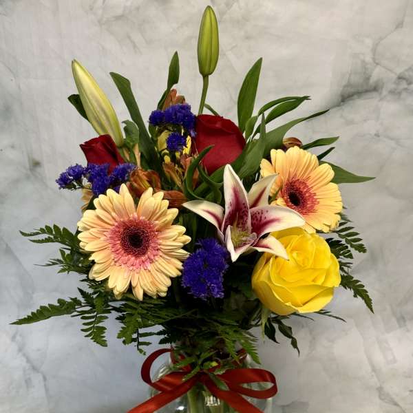Mixed bouquet in a glass vase with lilies, roses, and gerbera daisies