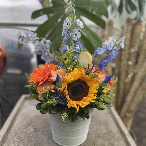 Bright mixed bouquet in a white metal bucket with a sunflower and blue flowers