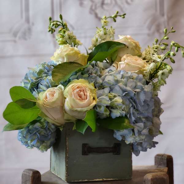 Blue hydrangeas and pale roses arranged in a green box
