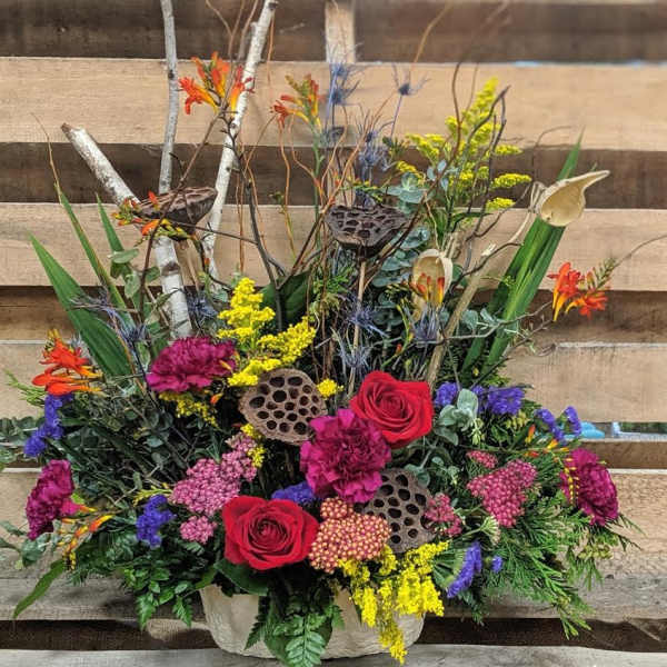 Colorful mixed floral arrangement with roses and calla lilies in a container