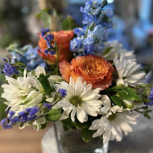 Bouquet of white daisies, orange roses, and blue flowers in a glass vase