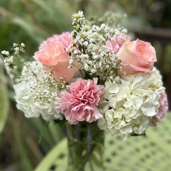 Pink roses and carnations in a clear glass vase with white hydrangeas