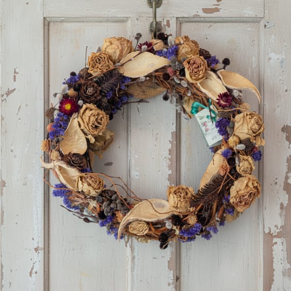 Dried floral wreath with tan roses and purple accents on a white door