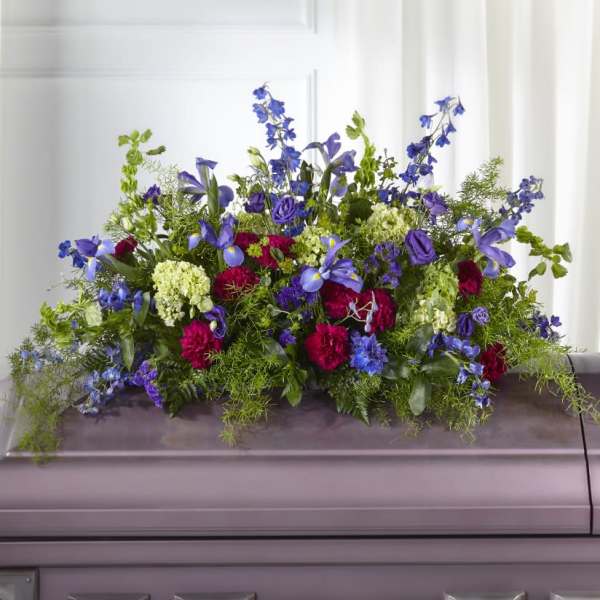 Large floral spray with blue, purple, pink, and white flowers on a casket