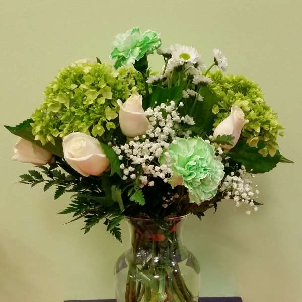 Bouquet of pale roses, green carnations, and white daisies in a glass vase