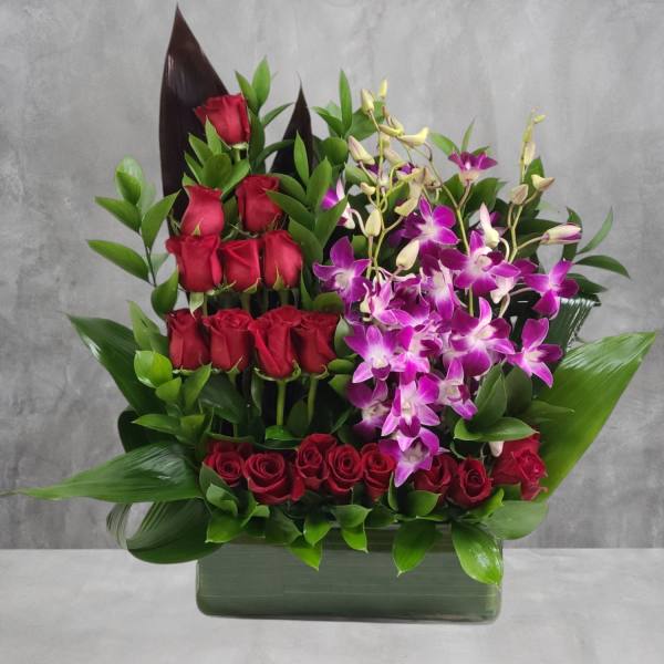 Red roses and purple orchids arranged in a rectangular vase