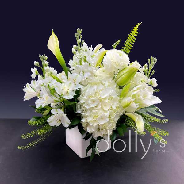 White floral arrangement in a square vase with lilies and hydrangeas