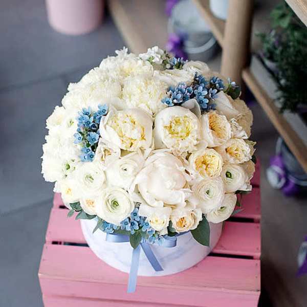 Round bouquet of white flowers with small blue accents in a white box