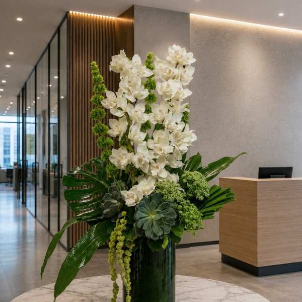 Tall white orchid arrangement in a dark glass vase with green tropical accents