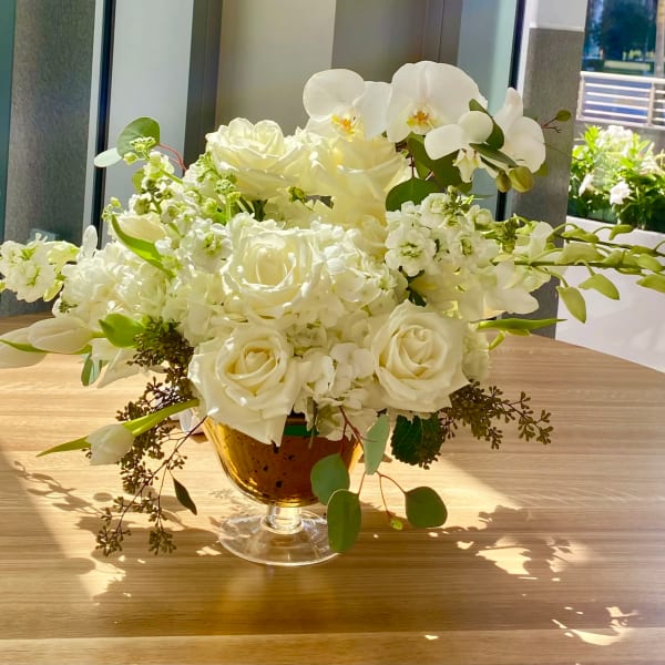 White roses and orchids arranged in a glass compote vase