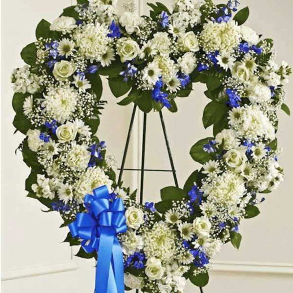 Heart-shaped white and blue floral wreath on a stand with a blue ribbon