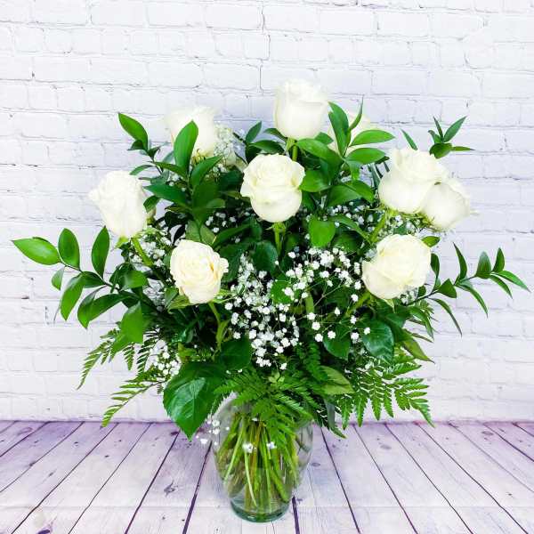 White roses in a glass vase with baby's breath and greenery