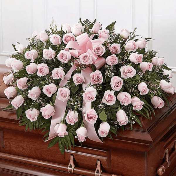 Pink rose casket spray with ribbon on a wooden coffin