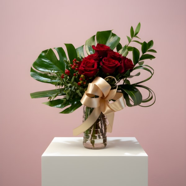 Arrangement of red roses with large glossy leaves in a glass vase tied with a gold bow