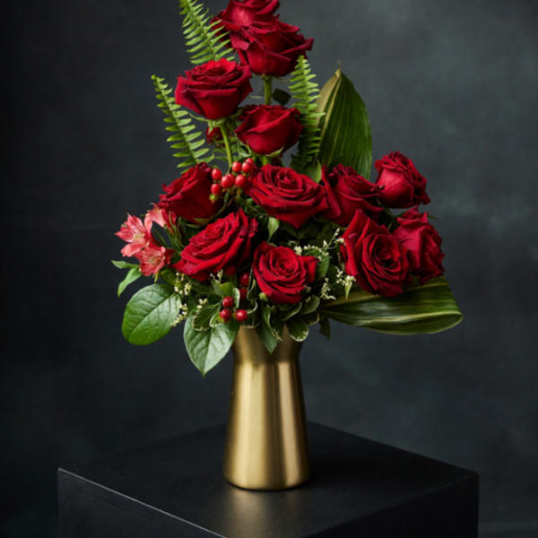Red roses arranged in a gold vase with green foliage