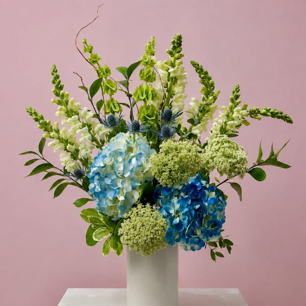 Blue and white hydrangeas in a white vase with tall green and white spikes