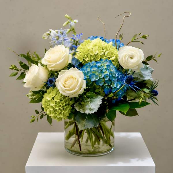 Blue and green floral arrangement with white roses in a glass vase