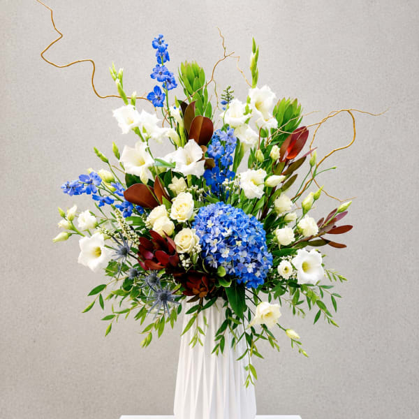 Tall floral arrangement with blue and white blooms in a white vase