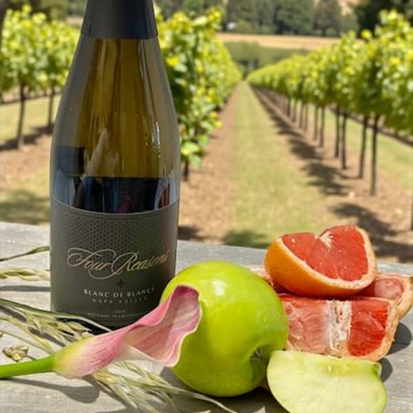 Wine bottle with fruit and a calla lily on a table outdoors