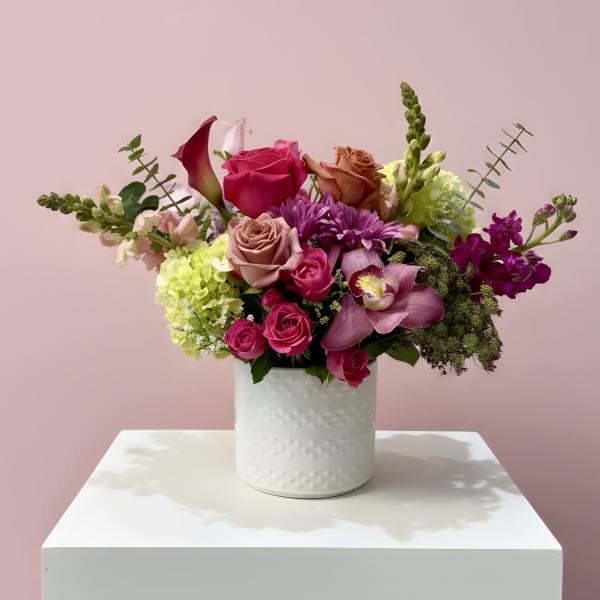 Mixed bouquet of pink, purple, and green flowers in a white vase