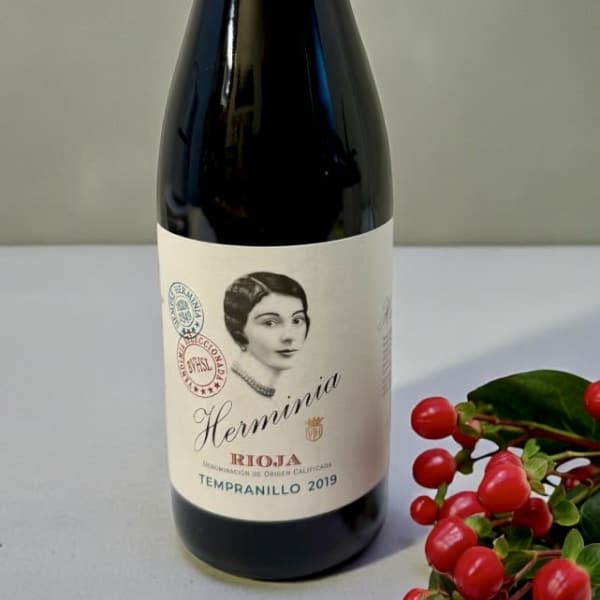 Bottle of red wine with a blue cap and berry sprig beside it