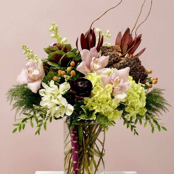 Mixed floral arrangement in a clear glass vase with pink orchids and green hydrangeas