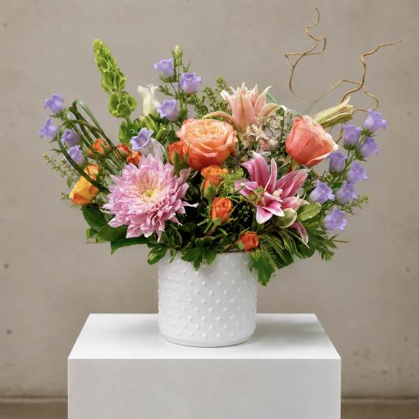 Mixed bouquet of pink, peach, purple, and white flowers in a white vase