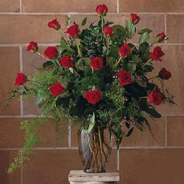 Tall arrangement of red roses with trailing greenery in a clear glass vase