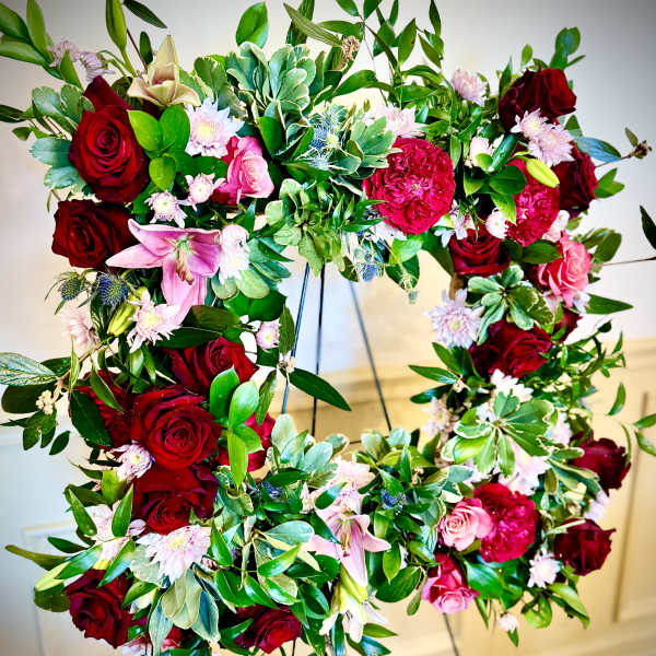 Standing wreath of red and pink flowers with lush green foliage on a metal easel.