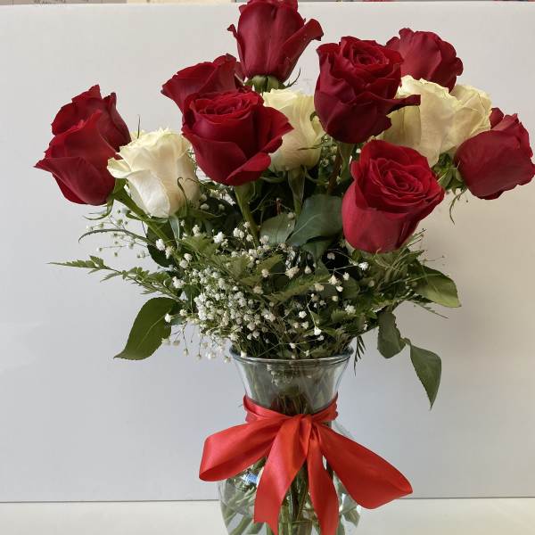 Arrangement of red and white roses with baby's breath in a clear glass vase tied with a red ribbon.