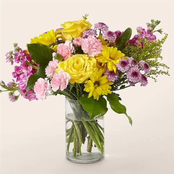 Mixed bouquet of yellow, pink, and purple flowers in a clear glass vase
