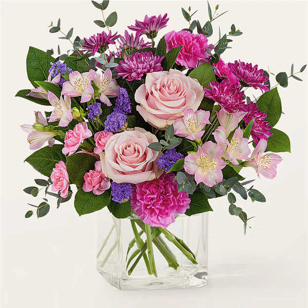 Bouquet of pink roses, carnations, and purple flowers in a clear glass vase
