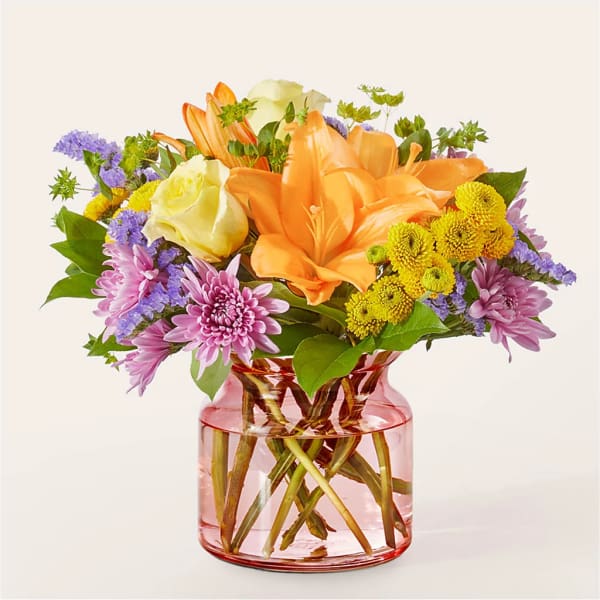 Orange lilies and mixed flowers in a pink glass vase