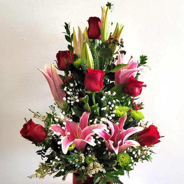Tall bouquet of red roses and pink lilies in a red glass vase