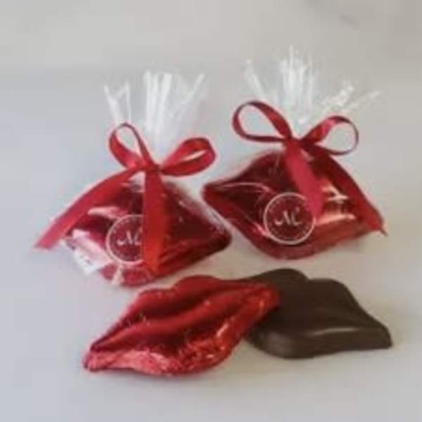 Two red ribbon-tied gift bags with chocolates and a red foil lips-shaped candy